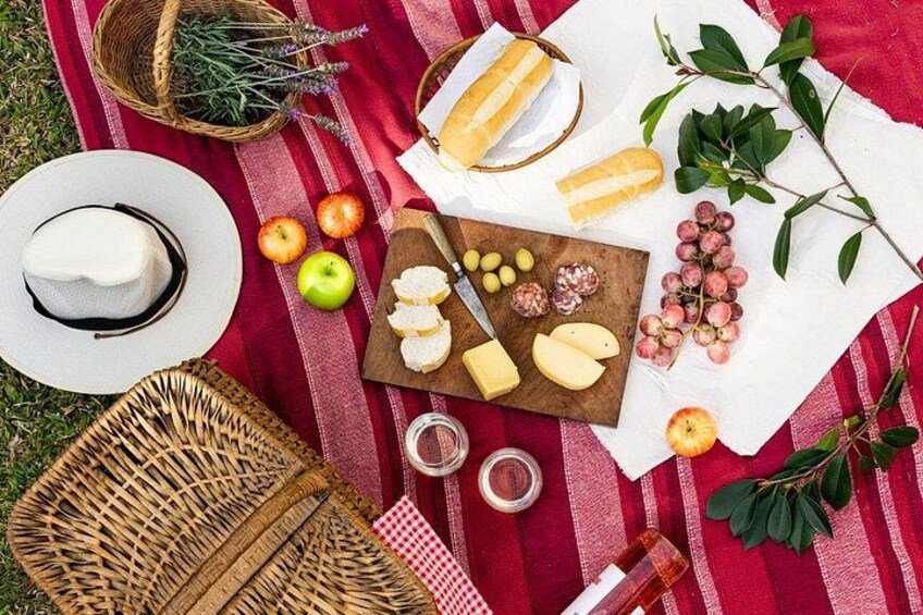 A picnic setup with a blanket, cheese, apples, grapes, and a basket. 2