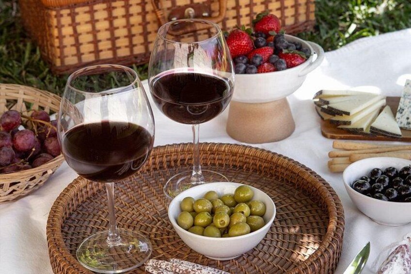 A picnic setup with wine glasses, bowls of grapes, olives, and cheese. 3