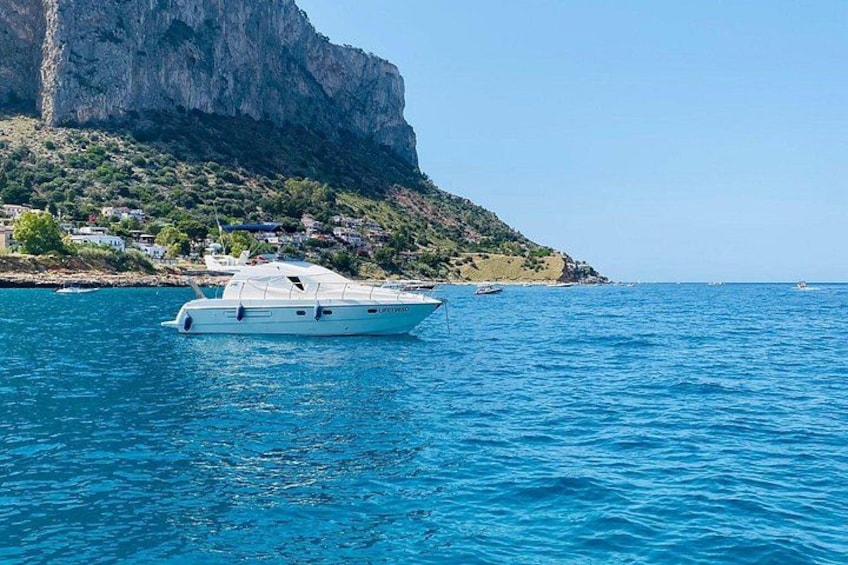 Un barco blanco sobre aguas azules tranquilas, con una costa rocosa y un acantilado al fondo. 2