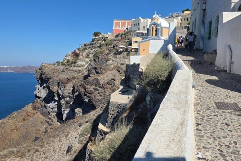 A coastal town with white buildings, a rocky cliff, and a clear blue sky. 2