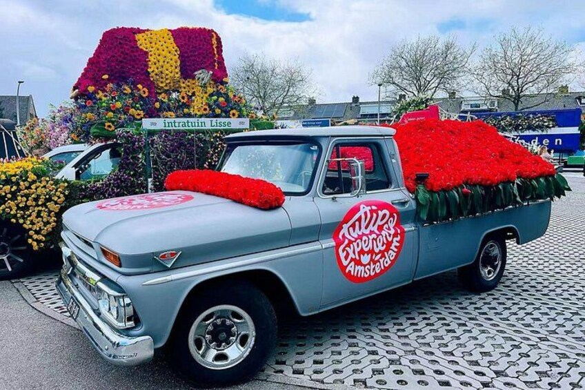 A vintage truck decorated with flowers and a red cushion, parked in a parking lot. 4
