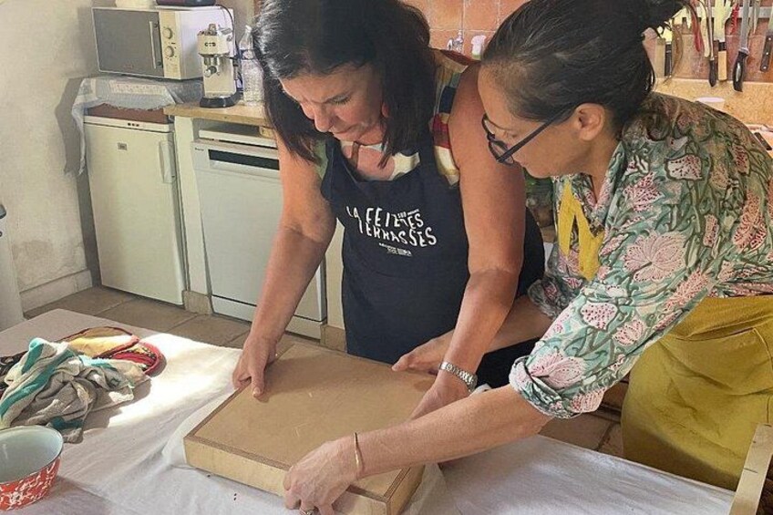Two people cutting a large piece of cardboard on a table in a kitchen. 1