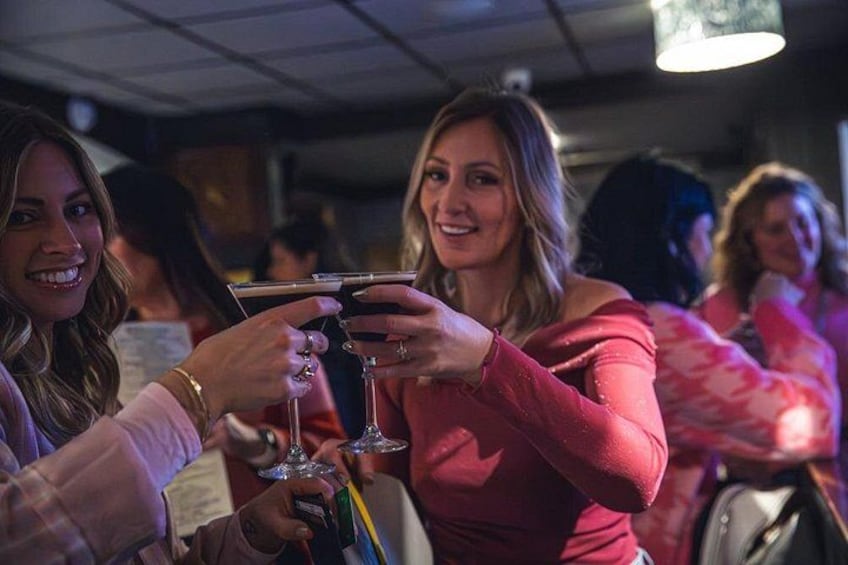 A group of people toasting with drinks in a dimly lit indoor setting. 4