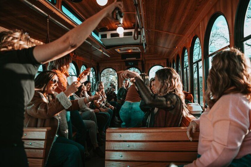 A group of people sitting on wooden benches inside a train car with arched windows. 5