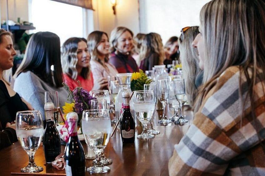 A group of people seated at a table with wine glasses and bottles. 3
