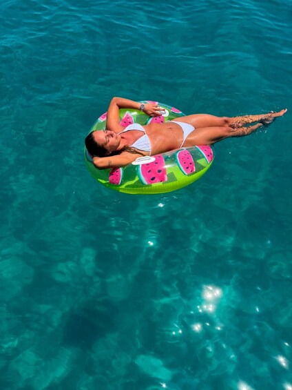 A person floating on a watermelon-themed inflatable in clear blue water. 1