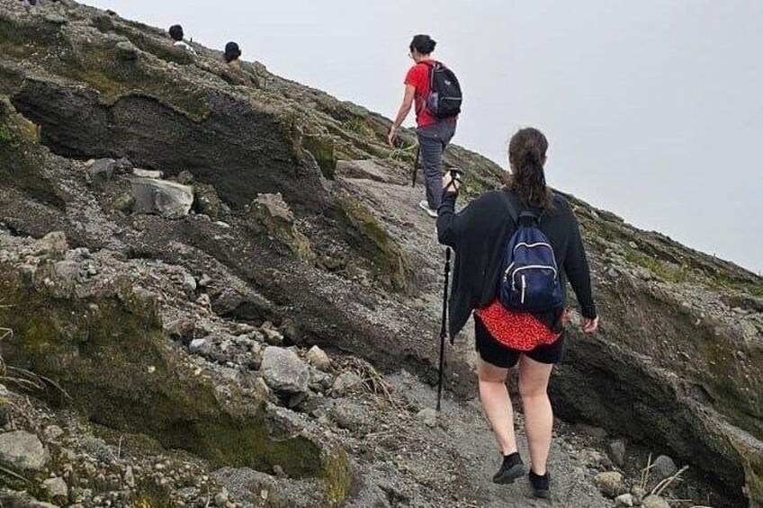 Des randonneurs gravissent une pente rocheuse, parsemée de rochers couverts de mousse et d’une végétation clairsemée. 5