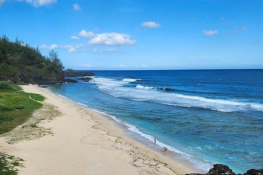 A beach with clear blue water, a sandy shore, and a rocky outcrop in the distance. 4