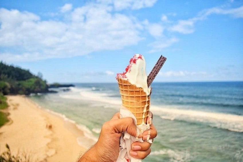 A hand holding an ice cream cone with a chocolate bar on a beach with ocean and sky in the background. 5