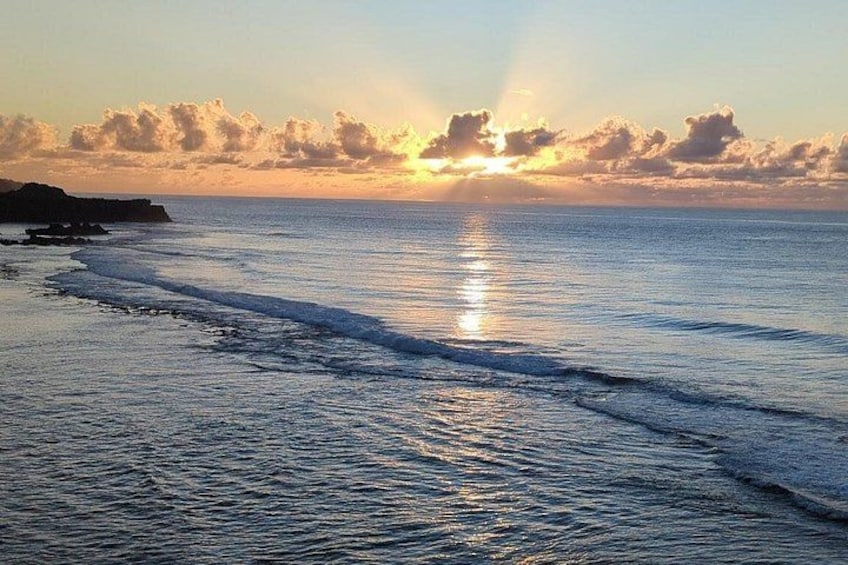 A sunset over a calm sea with waves, a rocky coastline, and scattered clouds. 2
