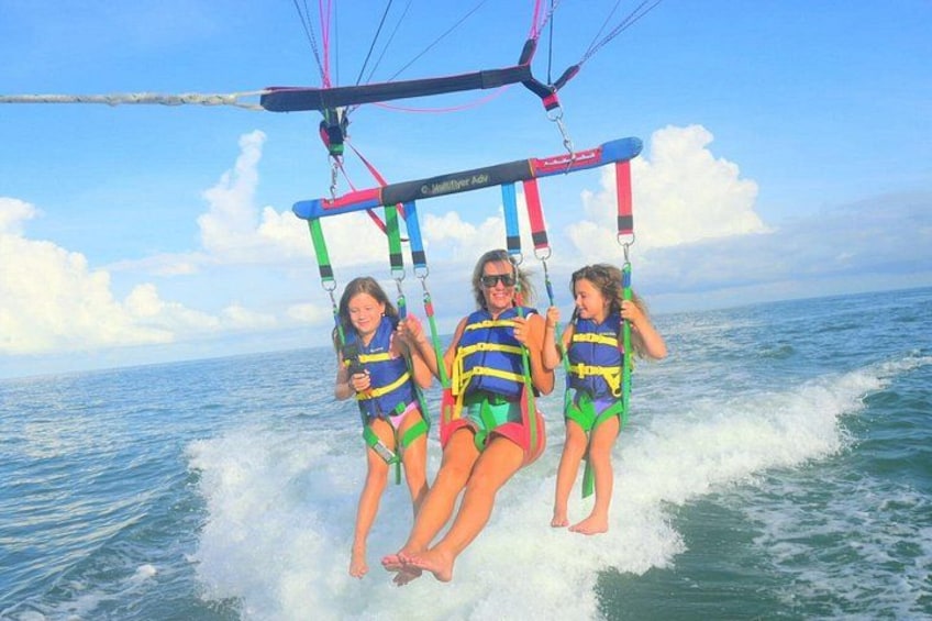 Tres personas practicando un deporte acuático, con chalecos salvavidas, y un cielo despejado y el océano al fondo. 3