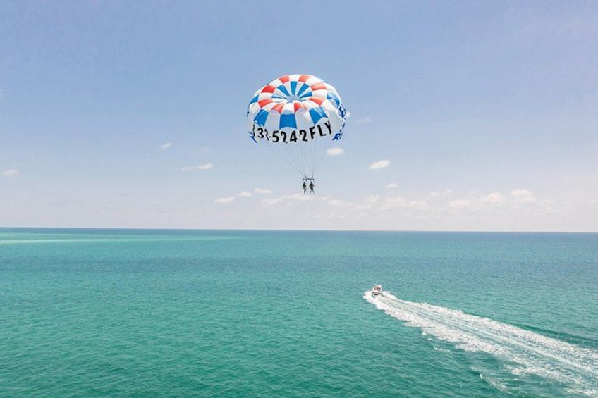 Un parapendio sobre un océano turquesa, un bote dejando estela y un cielo despejado. 1