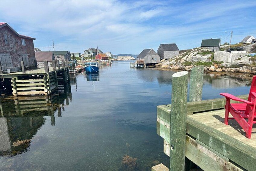 A calm waterway with a wooden dock, a red chair, and traditional buildings in a coastal village. 4