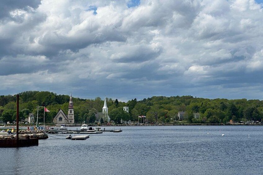 A harbor with boats, a church, and a forested hill. 2