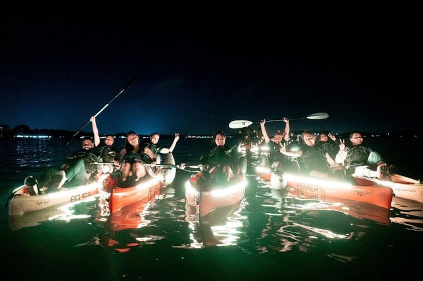 A group of people in a boat with lights on, rowing on a body of water at night. 3