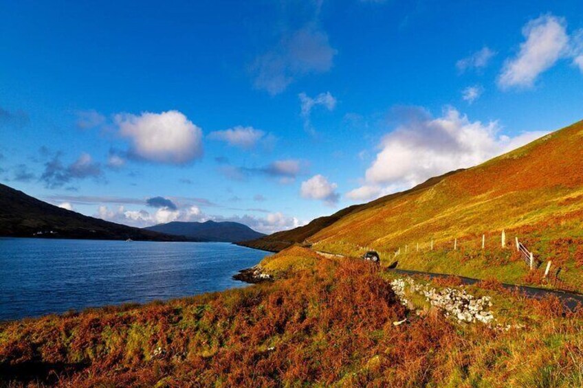 A lake with a road and fence, surrounded by hills and autumn foliage. 4