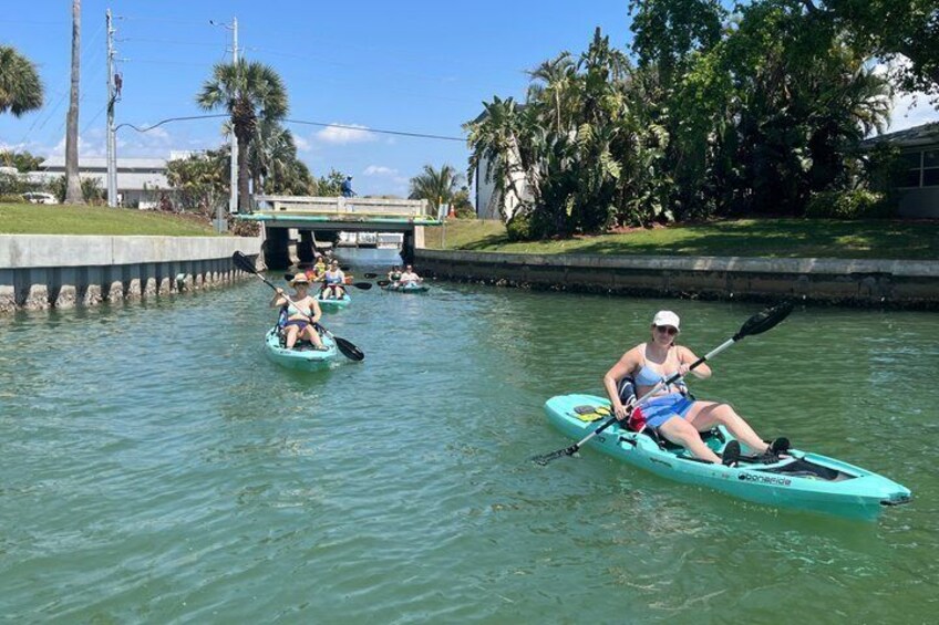 Persone che fanno kayak su un fiume tranquillo, circondate dal verde e con un ponte sullo sfondo. 4