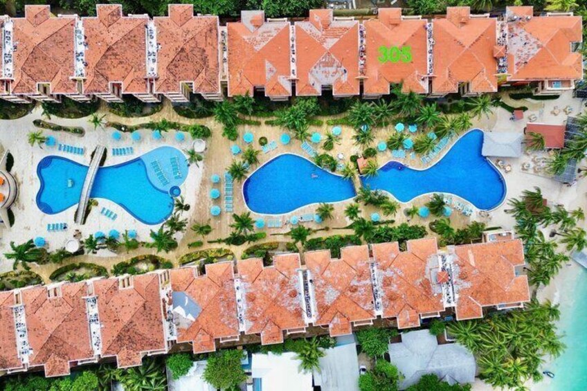 Et resort med flere swimmingpools, palmer og bygninger med terracotta tag. 2