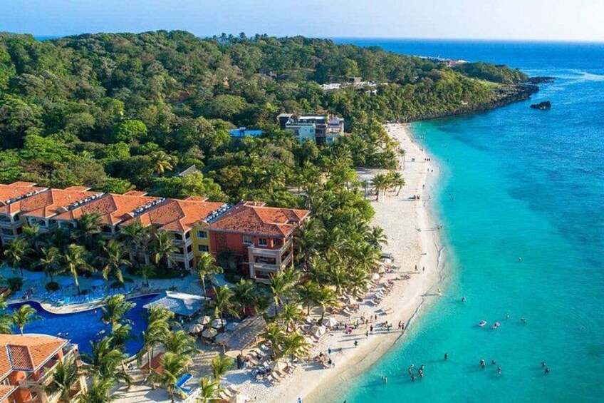 Un complejo turístico frente al mar con playa, piscina y abundante vegetación. 2