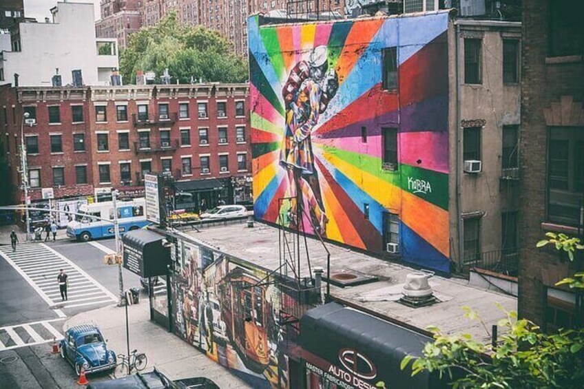 Un murale colorato su un edificio, una strada con auto e un attraversamento pedonale, e una bicicletta parcheggiata. 2