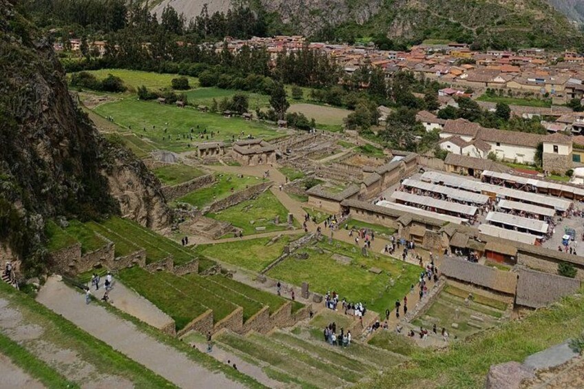 An archaeological site with ruins and pathways, surrounded by greenery and a mountainous backdrop. 5