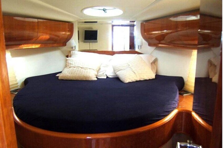 A compact, well-lit cabin with a bed, wooden cabinetry, and a television. 1