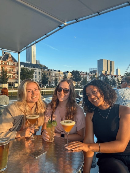 Three people sitting at a table with drinks, a cityscape in the background, and a clear sky. 1