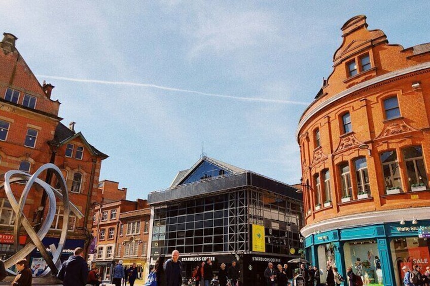 Ett livligt torg i stadskärnan med historiska byggnader, en modern byggnad med glasfasad och ett Starbucks. 3