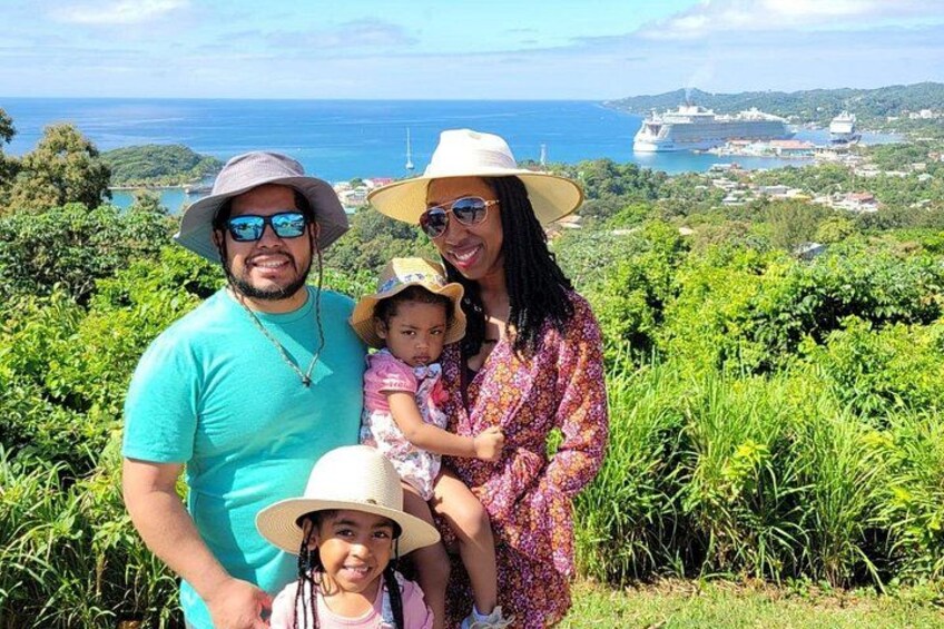 Una familia de tres personas en un paisaje verde y exuberante, con vista al océano y barcos a lo lejos. 4