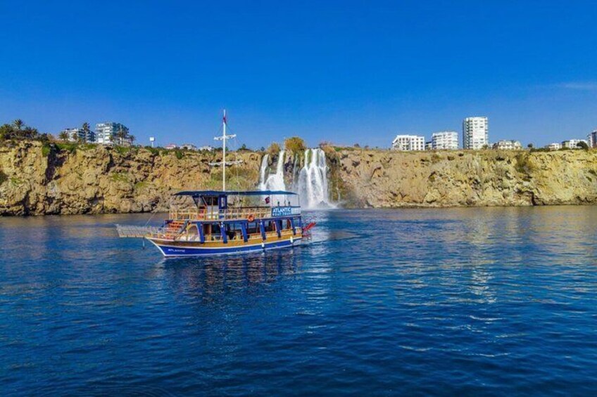 A boat named 'ATLANTIC' on calm water with a waterfall in the background and buildings on the shore. 1
