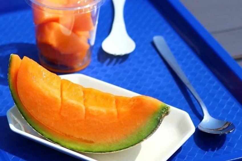 A cantaloupe on a white plate with a blue tray and a spoon in the background. 5