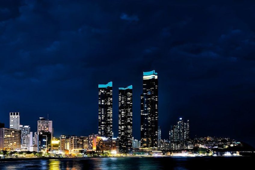 Un horizonte urbano nocturno con edificios iluminados y una masa de agua al frente. 3