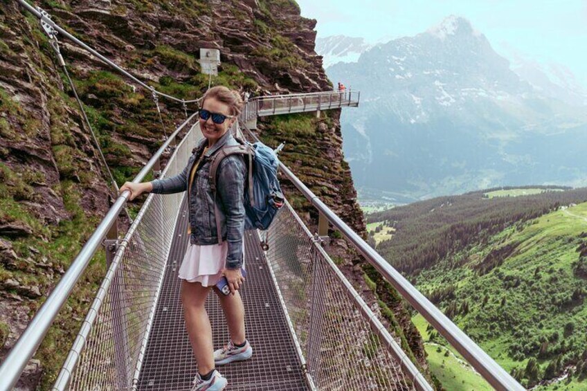 Una persona caminando sobre un puente de metal, con un paisaje montañoso al fondo. 1