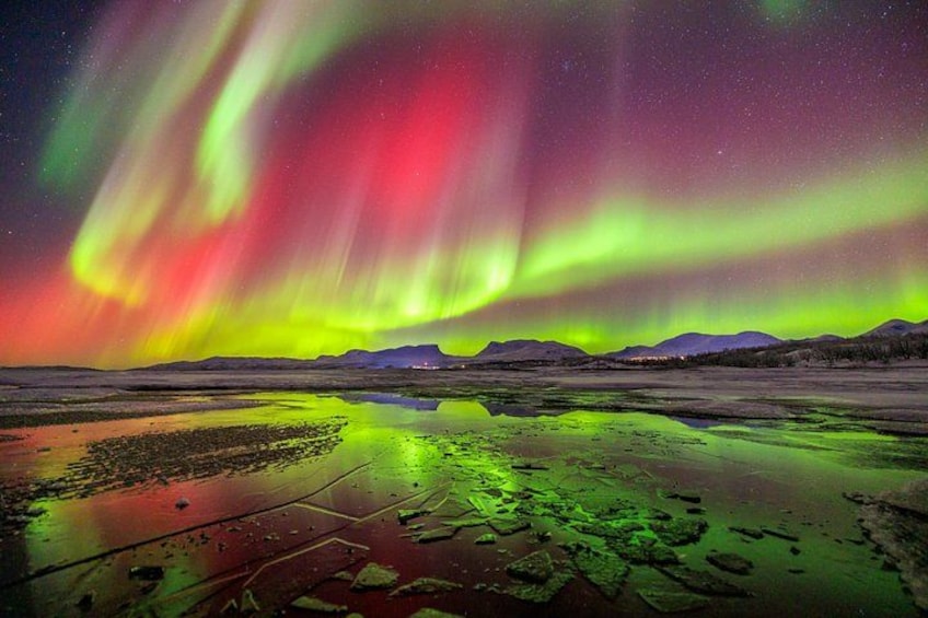 The Northern Lights over a reflective water surface with mountains in the background. 1
