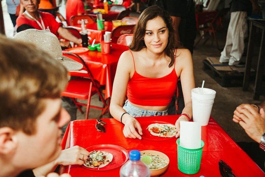 A person in a red top sitting at a red table with a drink and a plate of food. 2