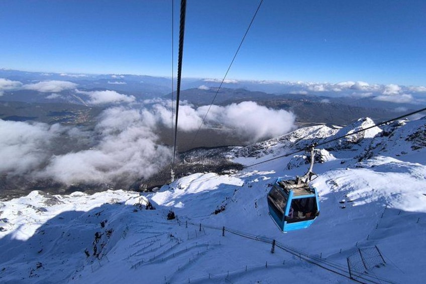 Un teleférico en una montaña nevada con cielo despejado y nubes abajo. 4