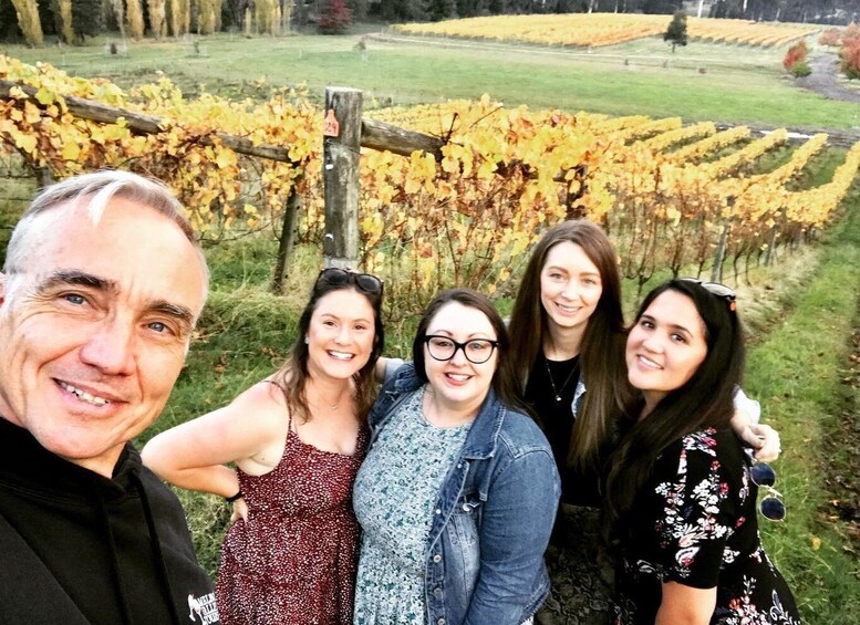 A group of people standing in a vineyard with rows of grapevines. 2
