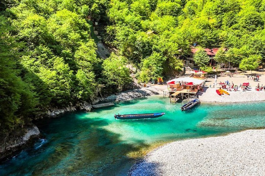 A turquoise river, boats, a beach with people, and a forested area. 1
