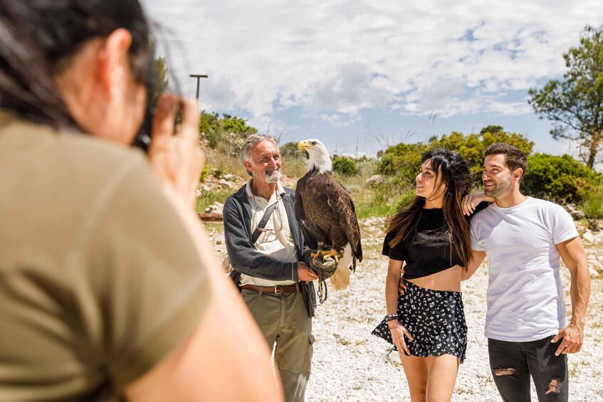A person holding a large bird, likely an eagle, with a group of people standing nearby in a natural outdoor setting. 2