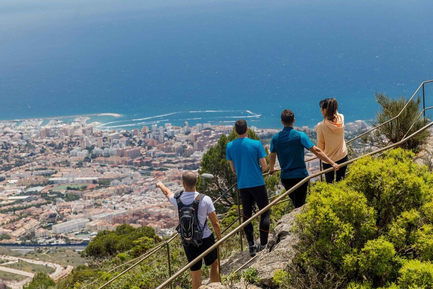 A group of people hiking on a trail with a city and coastline in the background. 4