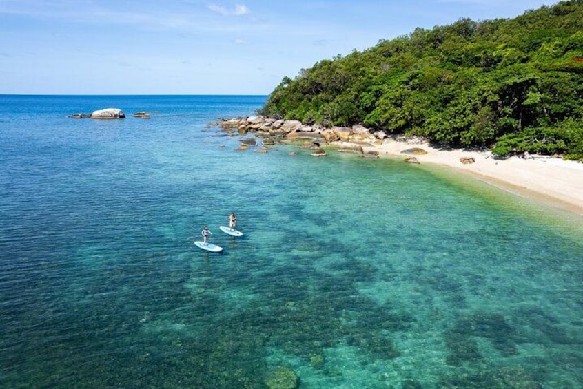 Una playa con agua turquesa cristalina, dos tablas de paddleboard y una colina boscosa. 2