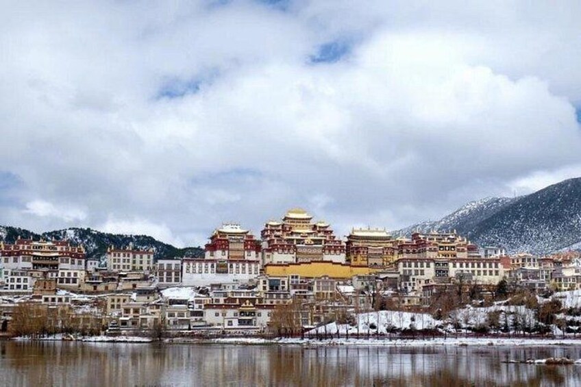 Paesaggio montuoso innevato con architettura tibetana tradizionale, tra cui un edificio giallo imponente con più livelli. 2