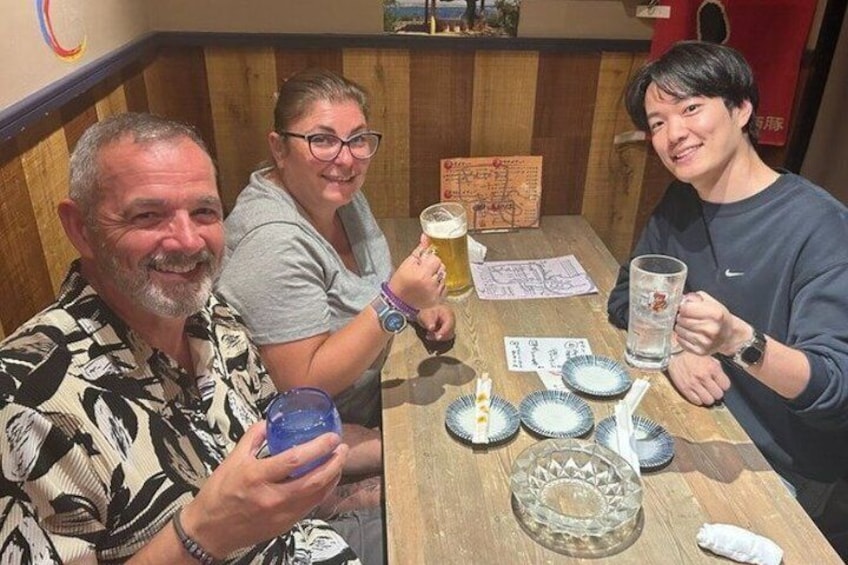 Three people seated at a wooden table with drinks and plates, in a restaurant setting. 5