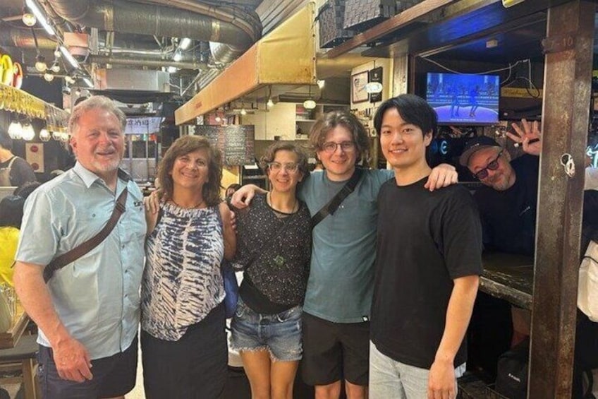 A group of people posing in a restaurant with a TV screen in the background. 4