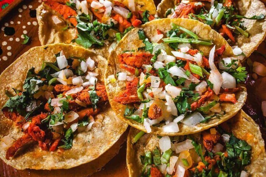 En närbild på flera tacos med färska tillbehör som lök, koriander och eventuellt kött. 2