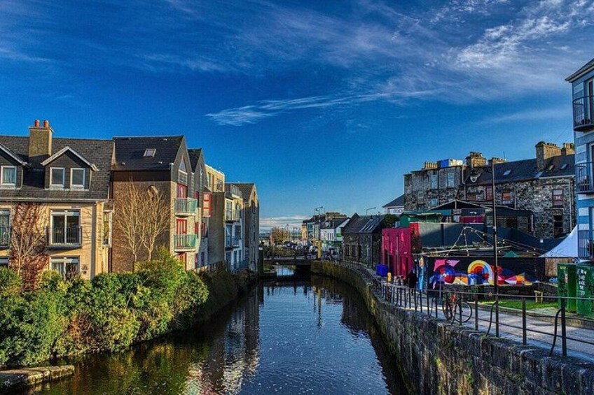 A canal with buildings on either side, a clear sky, and a colorful mural on the right. 2