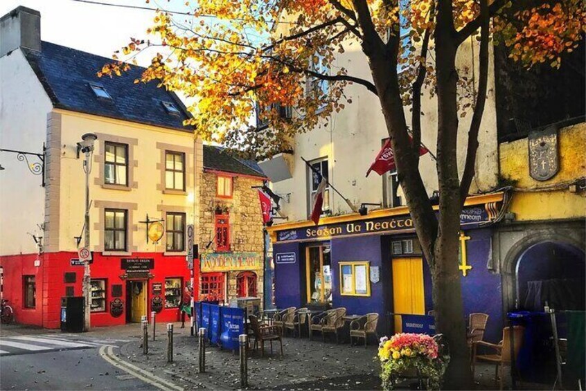 Een straat met kleurrijke gebouwen, waaronder een pub genaamd 'Station Da Neacra'. 3