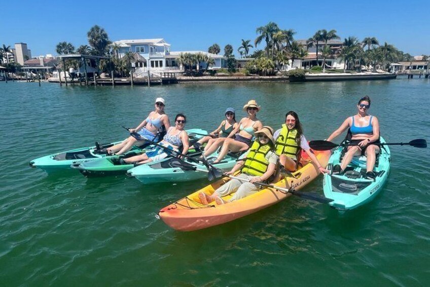 Un groupe de personnes fait du kayak sur une étendue d’eau calme, avec une promenade en bord de mer et des palmiers en arrière-plan. 4