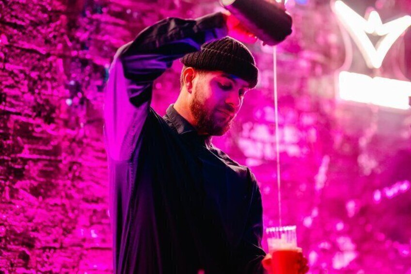 A person holding a drink with a neon sign in the background. 5