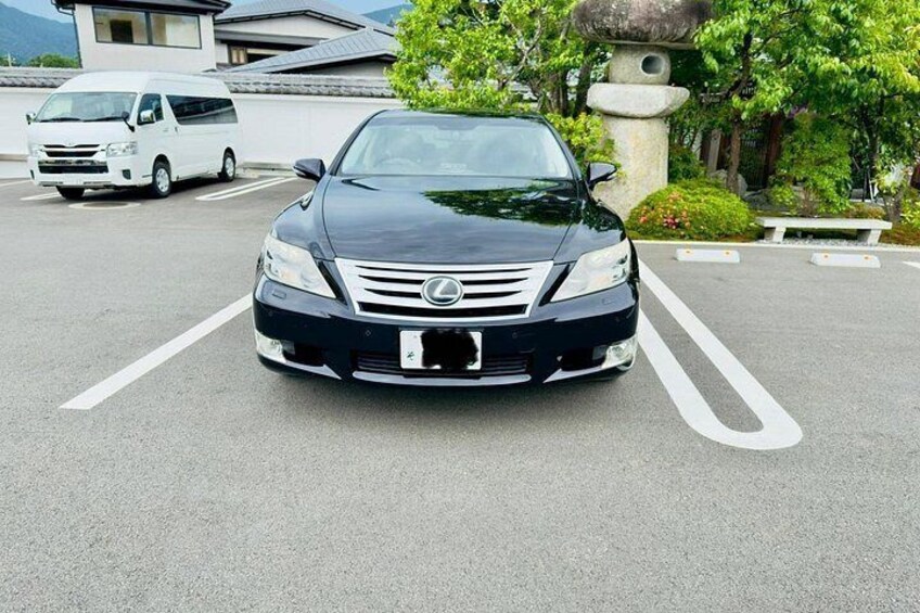 Un coche negro Lexus estacionado en un aparcamiento, con una furgoneta blanca al fondo. 4